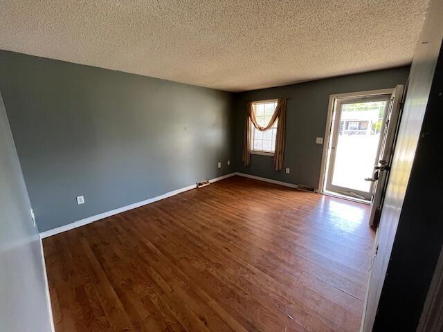 empty room with a textured ceiling, dark wood finished floors, and baseboards