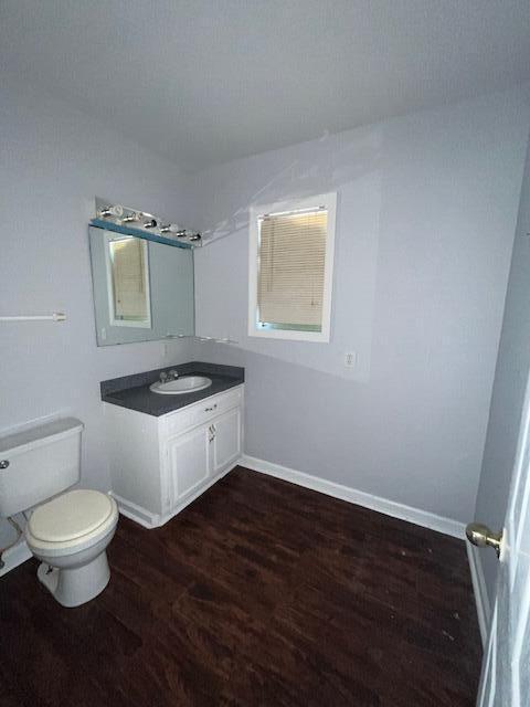 half bath featuring toilet, baseboards, wood finished floors, and vanity