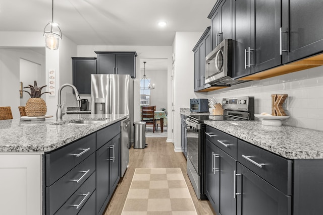 kitchen with a center island with sink, decorative light fixtures, stainless steel appliances, sink, and tasteful backsplash