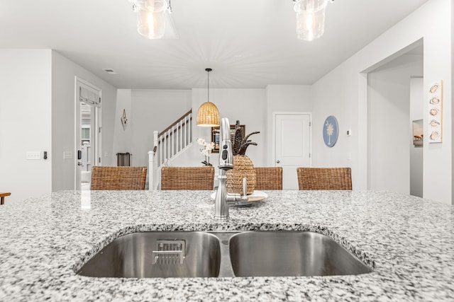 kitchen with decorative light fixtures, sink, and light stone countertops