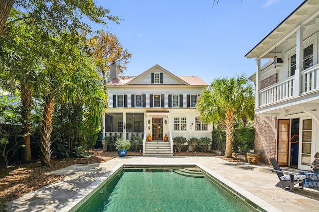 rear view of property featuring an outdoor pool, a sunroom, a patio, metal roof, and a chimney