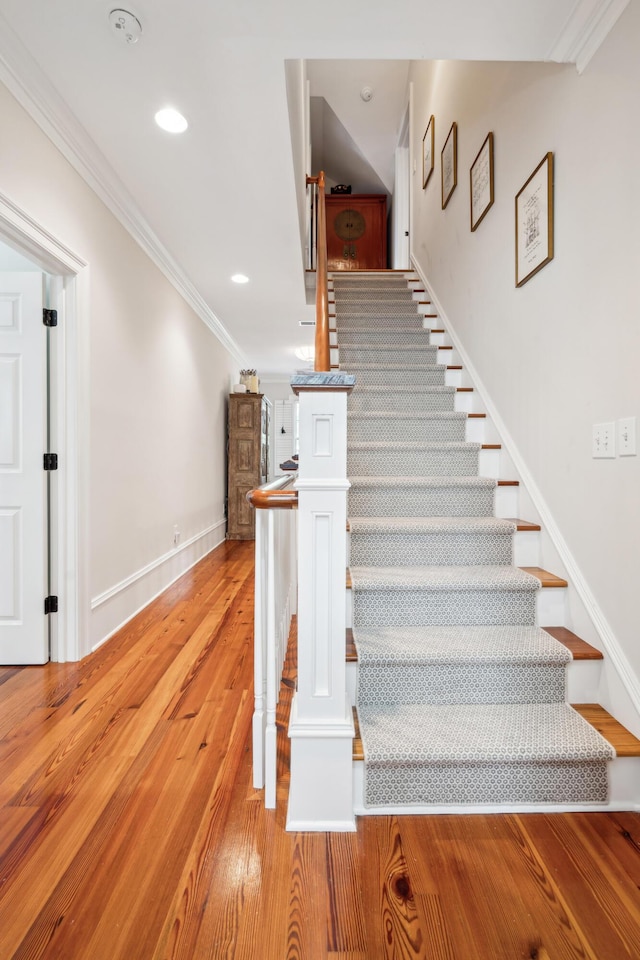 stairway with baseboards, crown molding, wood finished floors, and recessed lighting