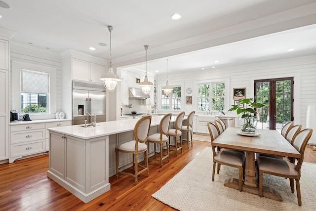 kitchen with light countertops, a sink, stainless steel built in fridge, light wood-style flooring, and under cabinet range hood