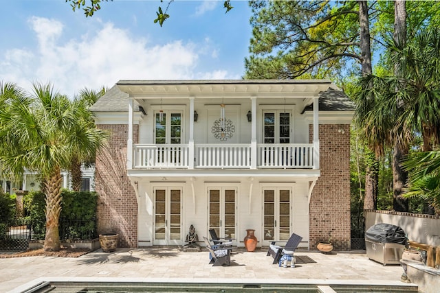 back of house with an outdoor pool, french doors, a balcony, brick siding, and a patio area