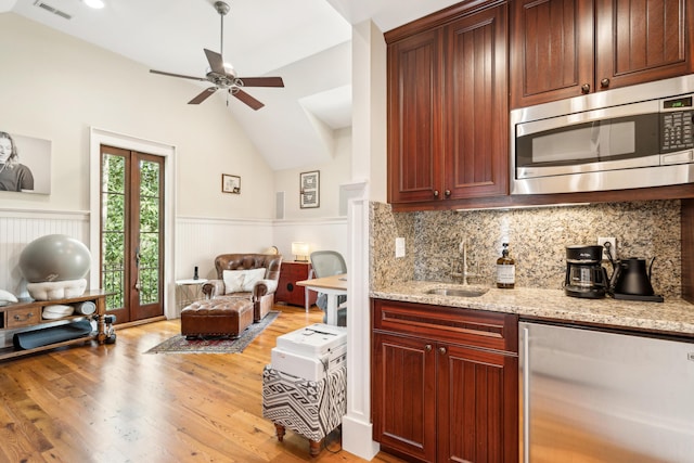kitchen with a wainscoted wall, ceiling fan, stainless steel microwave, refrigerator, and a sink