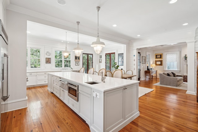 kitchen with light countertops, white cabinetry, an island with sink, a sink, and light wood-style floors