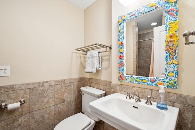 full bathroom featuring tile walls, a wainscoted wall, toilet, curtained shower, and a sink