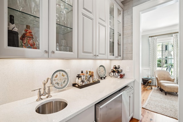 bar featuring a sink, a bar, wood finished floors, dishwasher, and ornamental molding