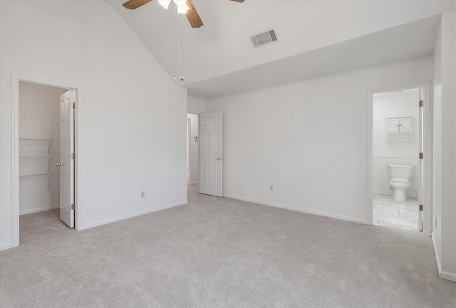 unfurnished bedroom with ensuite bath, a spacious closet, high vaulted ceiling, light carpet, and ceiling fan