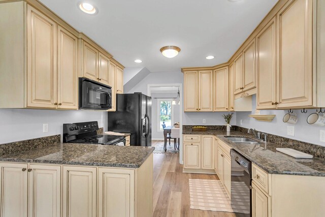 kitchen with light wood-type flooring, black appliances, dark stone counters, and sink