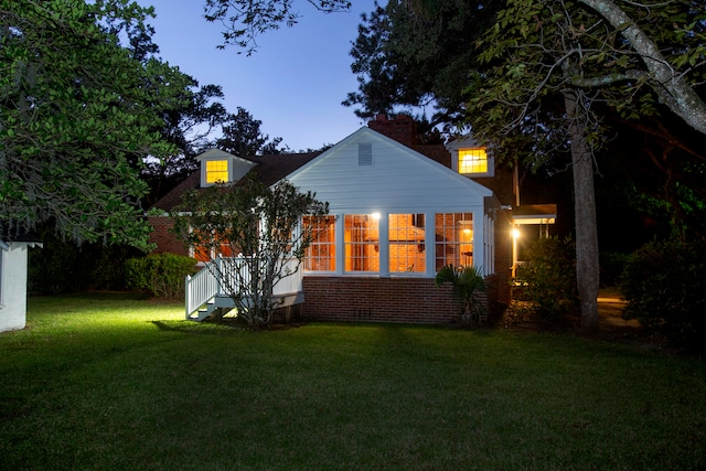 back house at dusk featuring a lawn and a sunroom