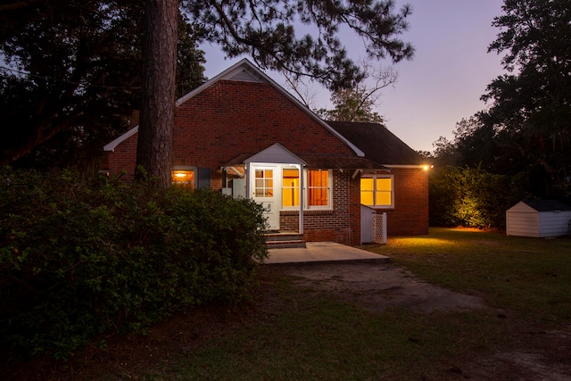 back house at dusk featuring a patio, a shed, and a yard