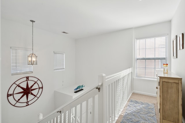 corridor with visible vents, baseboards, an inviting chandelier, carpet flooring, and an upstairs landing