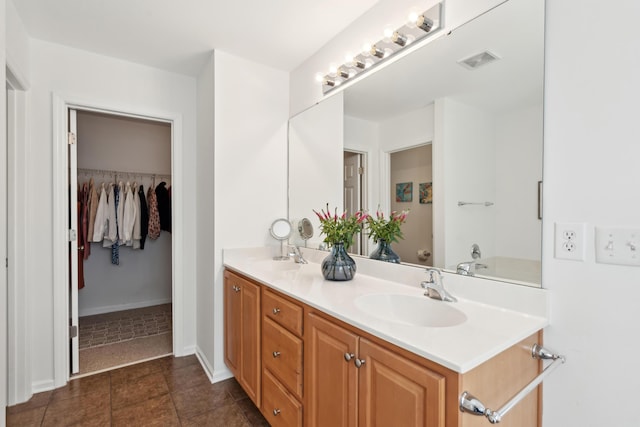 full bath featuring double vanity, visible vents, a walk in closet, and a sink