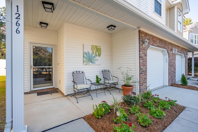 entrance to property with brick siding, driveway, a garage, and a patio