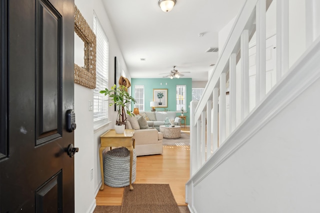 foyer with ceiling fan, visible vents, wood finished floors, and stairs