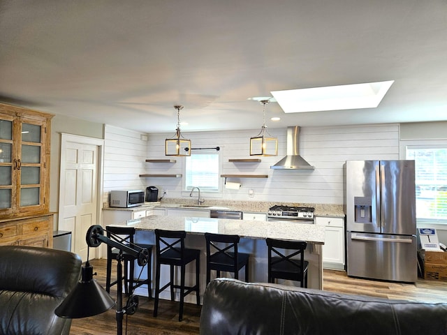 kitchen featuring a center island, stainless steel appliances, wall chimney range hood, pendant lighting, and a sink