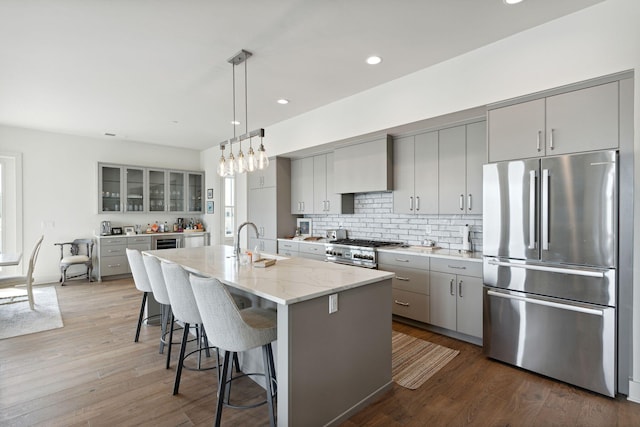 kitchen featuring appliances with stainless steel finishes, light stone countertops, wood-type flooring, decorative backsplash, and a center island with sink