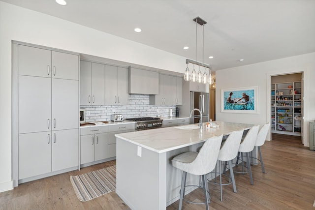 kitchen with decorative light fixtures, a center island with sink, stainless steel appliances, decorative backsplash, and light wood-type flooring