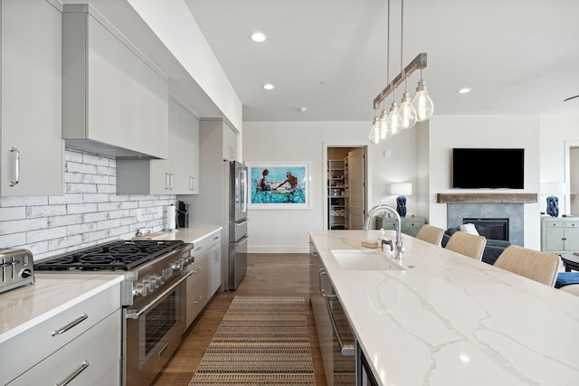 kitchen with pendant lighting, sink, light stone countertops, dark wood-type flooring, and appliances with stainless steel finishes