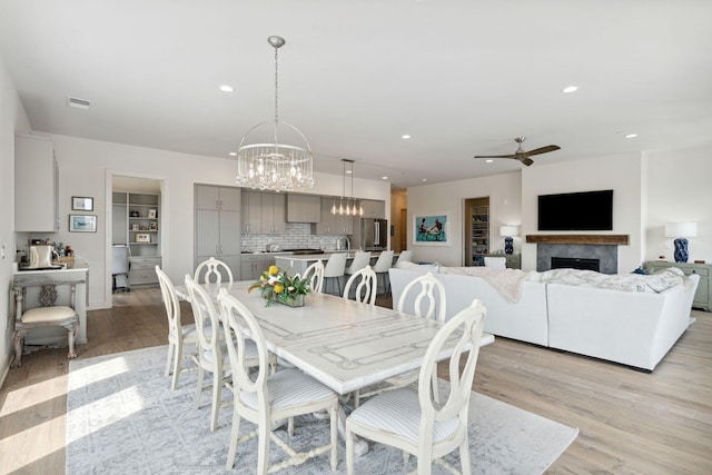 dining space with ceiling fan with notable chandelier, a fireplace, and light hardwood / wood-style floors