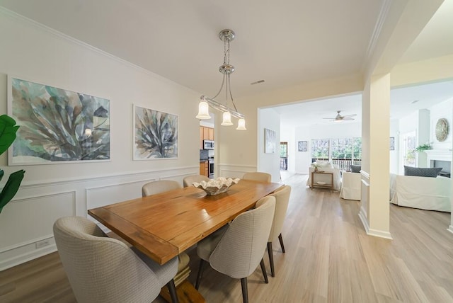 dining space featuring a wainscoted wall, crown molding, a decorative wall, and light wood finished floors