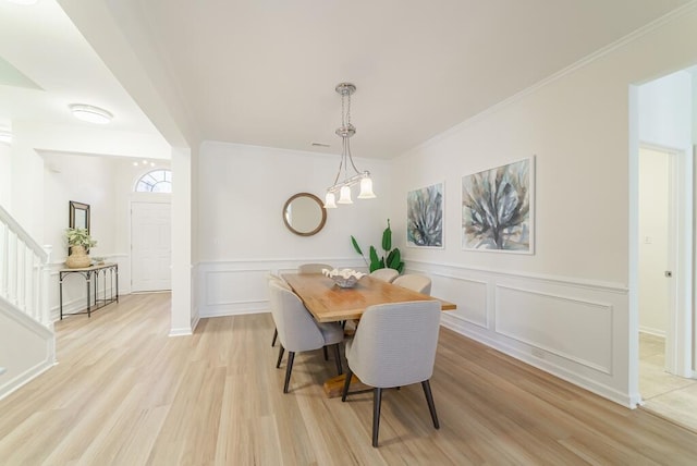 dining area featuring a decorative wall, stairway, light wood-style floors, ornamental molding, and a chandelier