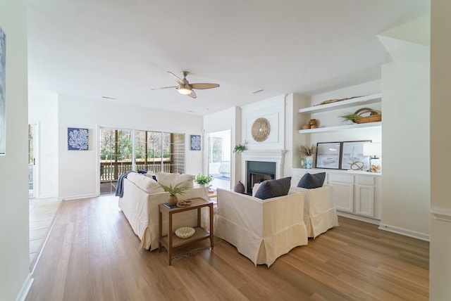 living room featuring ceiling fan, a fireplace, baseboards, and light wood-style floors