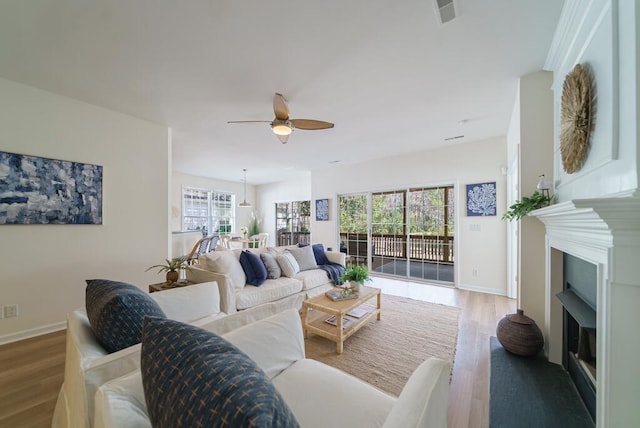 living room with a fireplace, wood finished floors, visible vents, and a ceiling fan