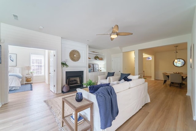 living area featuring ceiling fan, light wood finished floors, and a fireplace with flush hearth