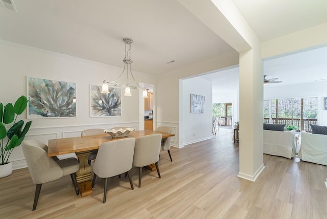 dining room featuring visible vents, wainscoting, ceiling fan, light wood-style floors, and a decorative wall