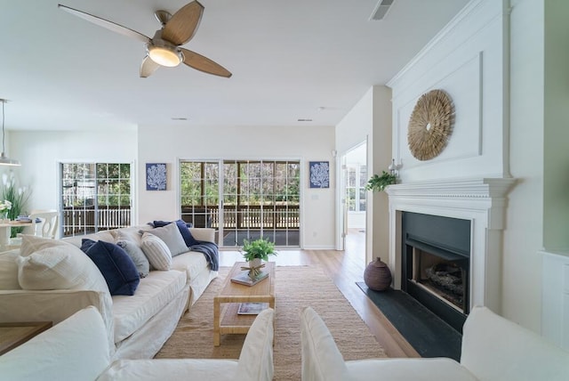 living room featuring a fireplace with flush hearth, visible vents, ceiling fan, and wood finished floors