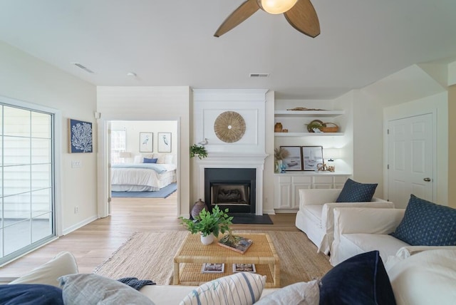 living area featuring light wood-style flooring, a fireplace, visible vents, and built in features