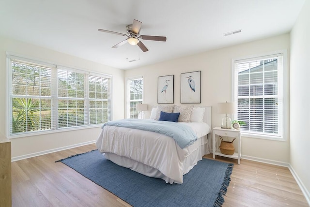 bedroom with a ceiling fan, visible vents, baseboards, and wood finished floors