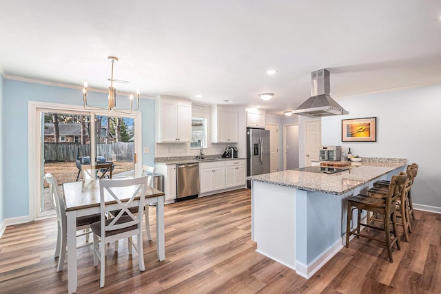 kitchen featuring decorative backsplash, appliances with stainless steel finishes, white cabinets, wall chimney range hood, and a peninsula