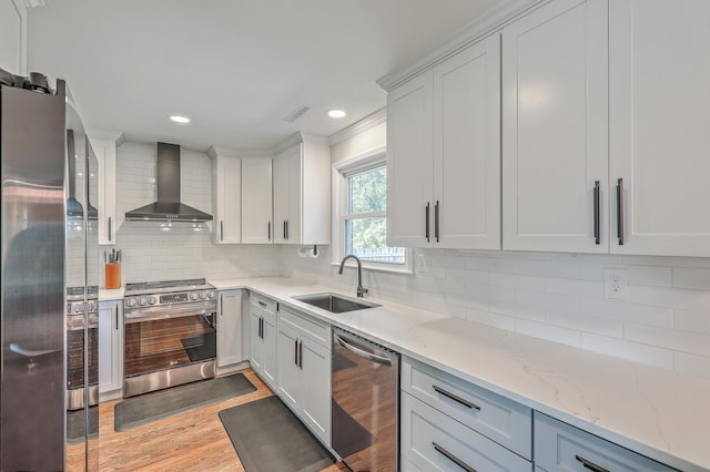 kitchen with sink, wall chimney range hood, decorative backsplash, white cabinets, and appliances with stainless steel finishes