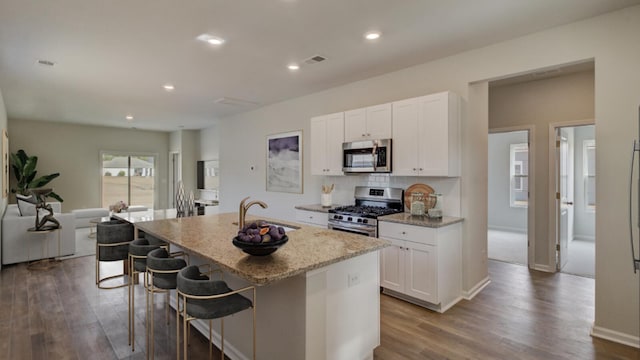 kitchen with light stone counters, a kitchen island with sink, stainless steel appliances, a sink, and visible vents