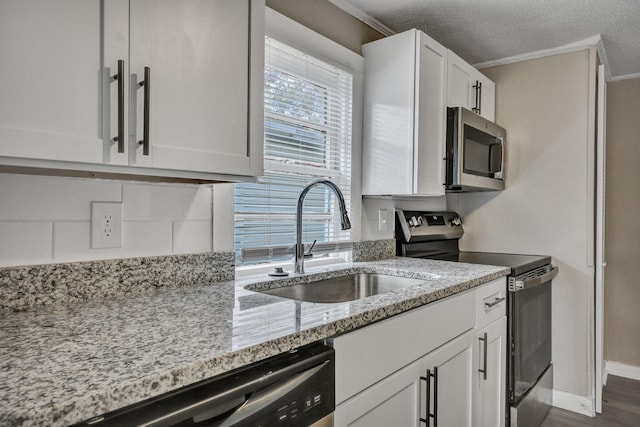 kitchen with sink, white cabinetry, ornamental molding, stainless steel appliances, and light stone countertops