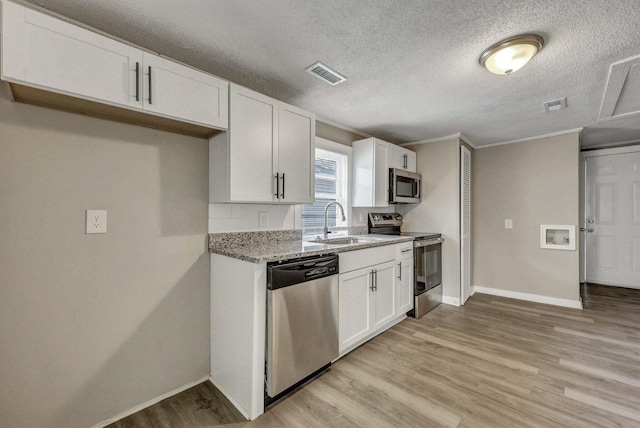 kitchen featuring sink, light hardwood / wood-style flooring, appliances with stainless steel finishes, white cabinetry, and light stone counters