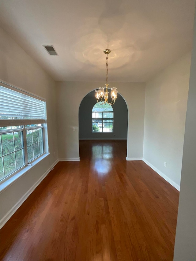 empty room with a notable chandelier and dark hardwood / wood-style flooring