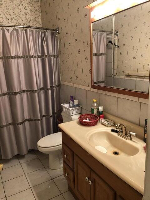 bathroom with tile patterned floors, toilet, tile walls, vanity, and curtained shower