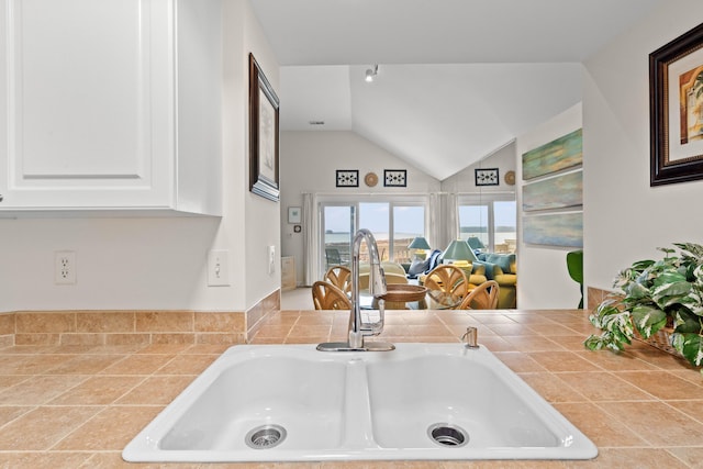 kitchen with a sink, open floor plan, tile countertops, white cabinets, and lofted ceiling