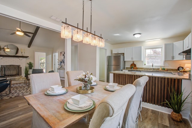 dining space featuring dark wood-style floors, a brick fireplace, vaulted ceiling with beams, and a ceiling fan