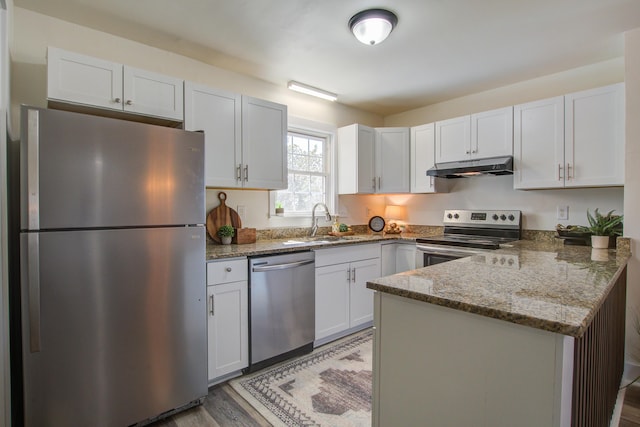 kitchen with under cabinet range hood, stainless steel appliances, a peninsula, a sink, and dark stone counters