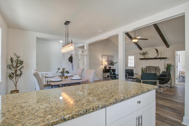 kitchen featuring white cabinets, hanging light fixtures, a brick fireplace, light stone countertops, and dark wood-style floors