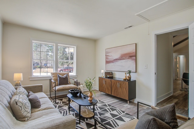 living room with visible vents, light wood-type flooring, attic access, and baseboards