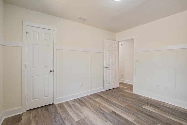 unfurnished bedroom featuring visible vents, a wainscoted wall, wood finished floors, a decorative wall, and a closet