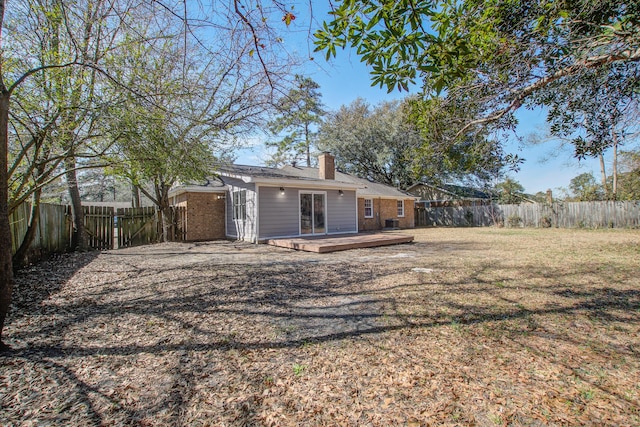 rear view of house with a deck, a fenced backyard, brick siding, a lawn, and a chimney