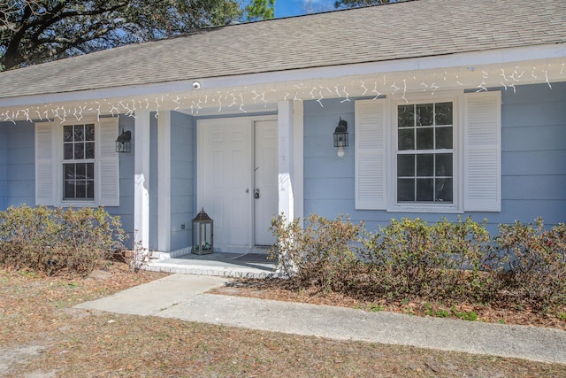 view of exterior entry with covered porch and roof with shingles