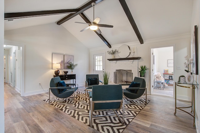 living area with ceiling fan, wood finished floors, baseboards, a brick fireplace, and beam ceiling